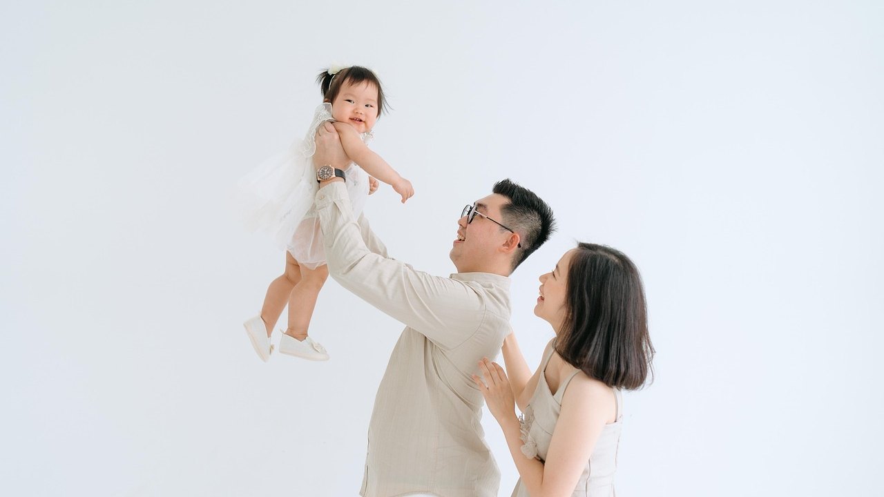 子どもを抱き上げる父親と見守る母親。育休と育児時短就業の制度改定を伝えるイメージ